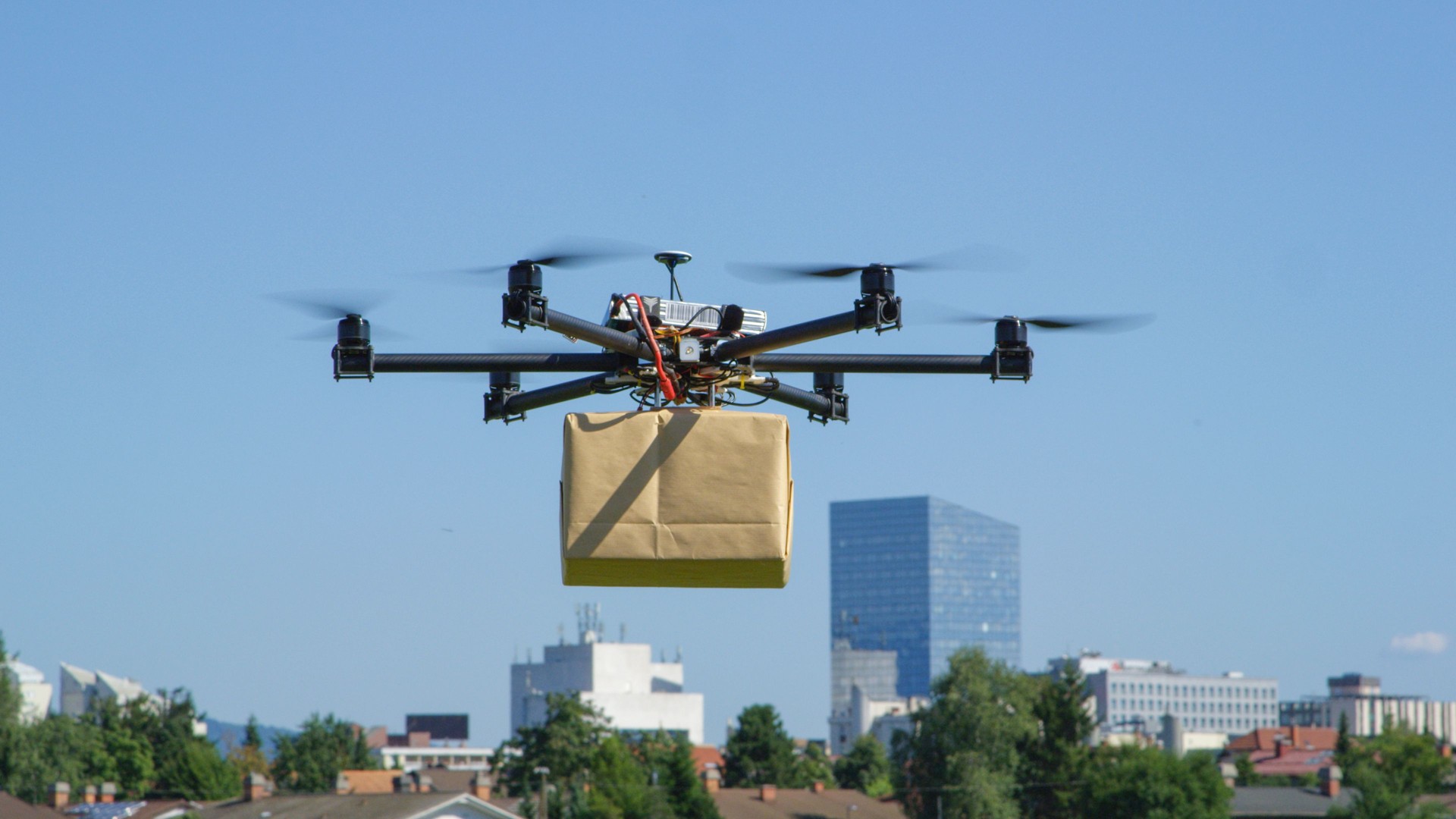 CLOSE UP: UAV drone delivery delivering big brown post package into urban city